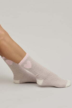Gray fuzzy socks with pink hearts worn by a person on a light gray background