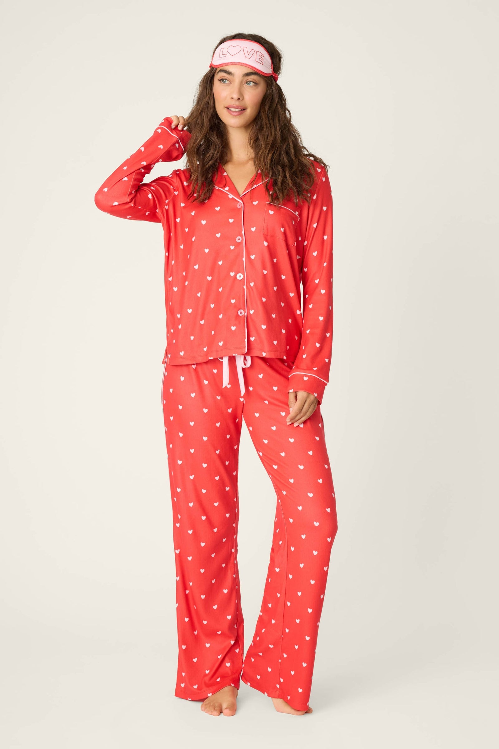 Woman wearing a red polka dot pajama set with a matching eye mask on a white background